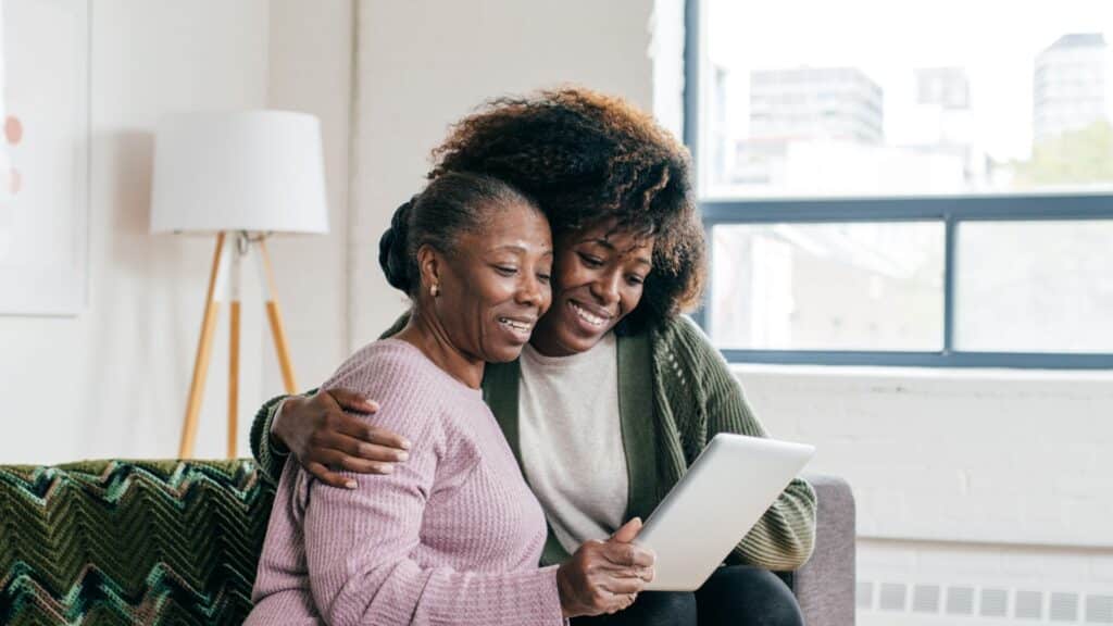Two women sit comfortably on a couch, focused on a tablet